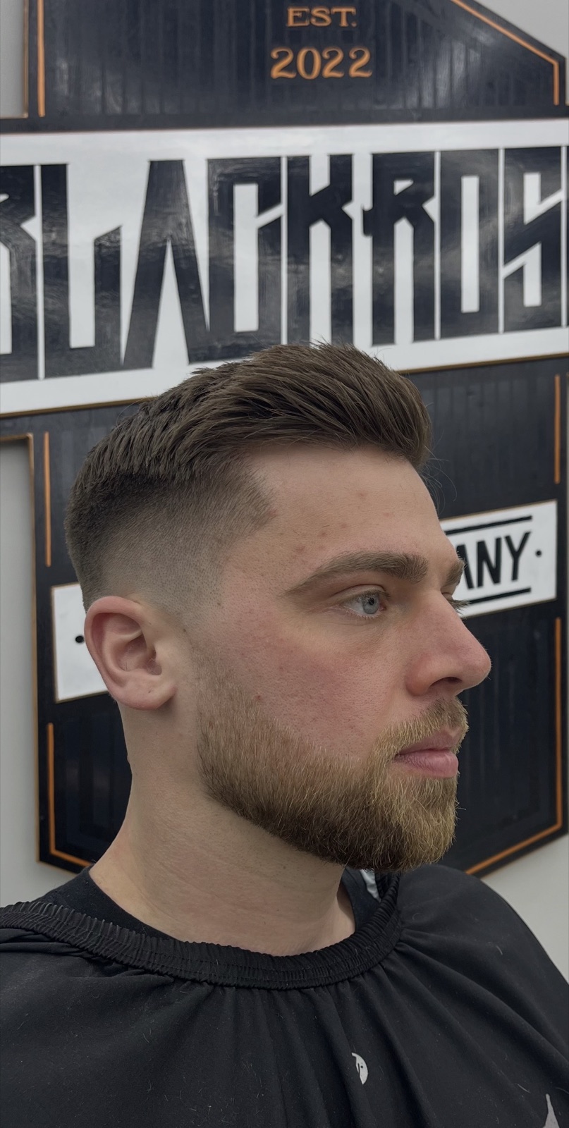 Brushed-up quiff and drop fade, in front of the shop sign