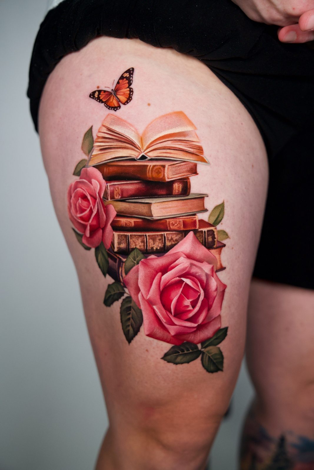 Stacked books, roses and a monarch butterfly on the thigh
