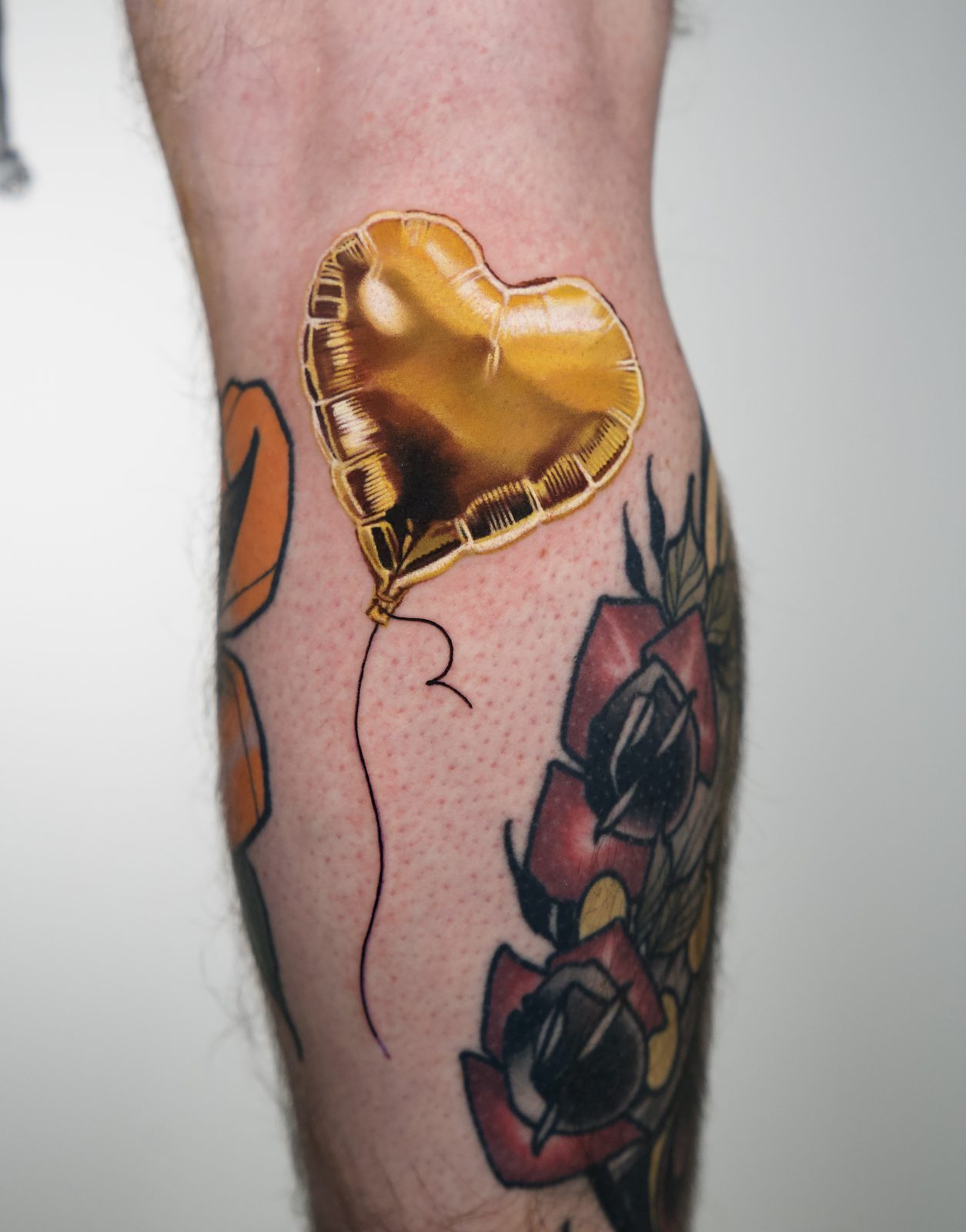 Gold heart balloon above dark red roses, on the calf